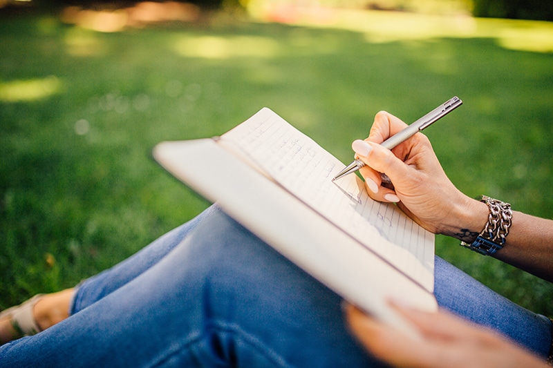 Female entrepreneur writing in a notebook in a green field