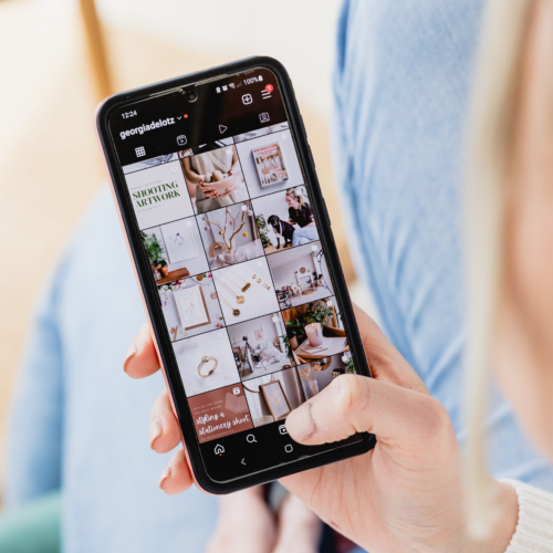 Woman holding phone in hand with phone screen showing Instagram profile grid.